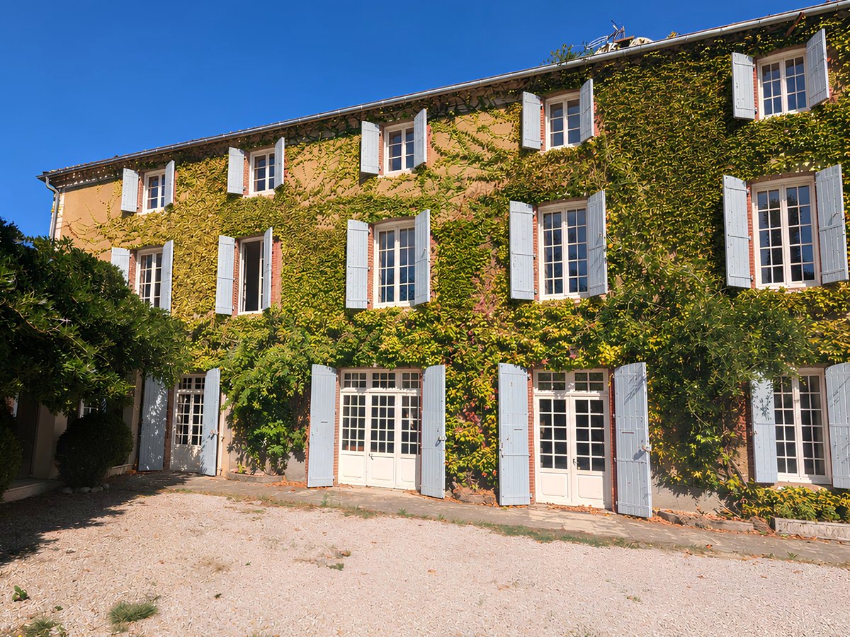 La façade de la maison couverte de vigne vierge rousse en automne, entre les arbres du parc