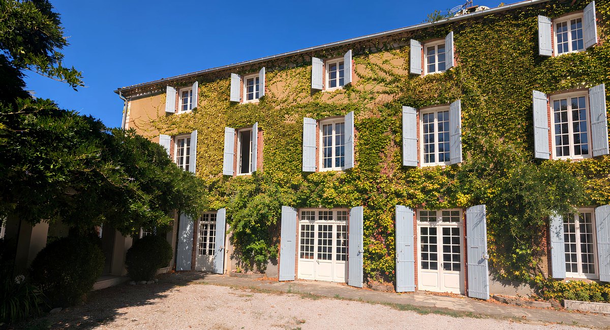 La façade de la maison de maître, tous volets ouverts et portes-fenêtres ouvertes, sous la vigne vierge